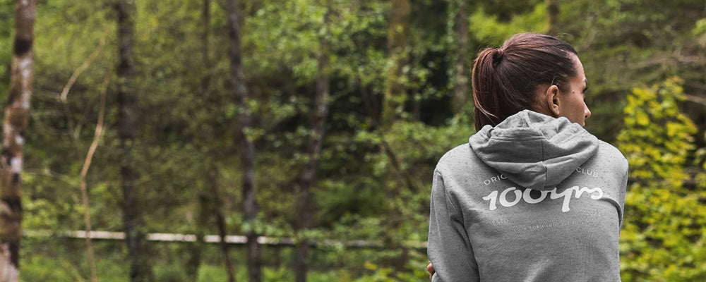 a woman wearing a light grey hoodie looking out over a forest